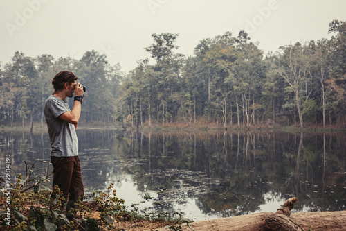 Traveller photographer standing and do pictures of tropical lake landscape by compact professional camera