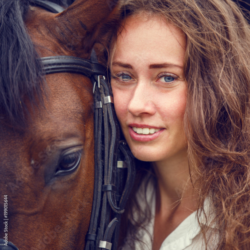 Young happy rider woman with her bay horse. Portrait of smiling girl with her stallion
