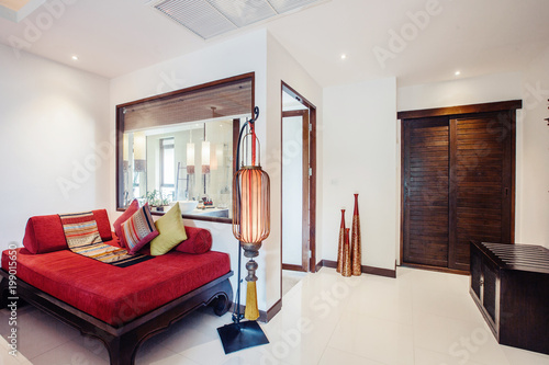 Modern bed room interior in expensive tropical hotel resort . Red sofa, big red lamp, wooden door and bathroom with big window