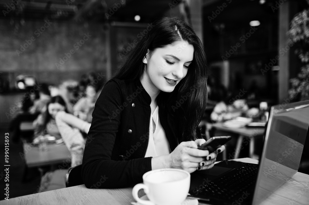 Brunette girl sitting on cafe with cup of cappuccino, working with red laptop and looking at mobile phone. Brunette girl sitting on cafe with cup of cappuccino, working with red laptop and looking at mobile phone.