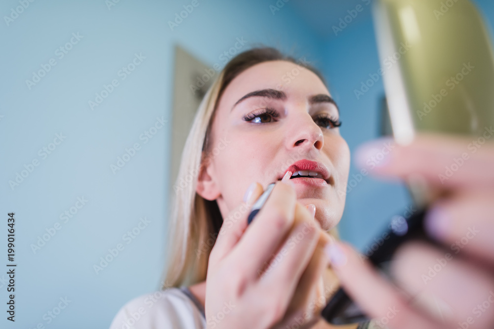 Young woman applying lipstick looking at mirror Young woman applying lipstick looking at mirror