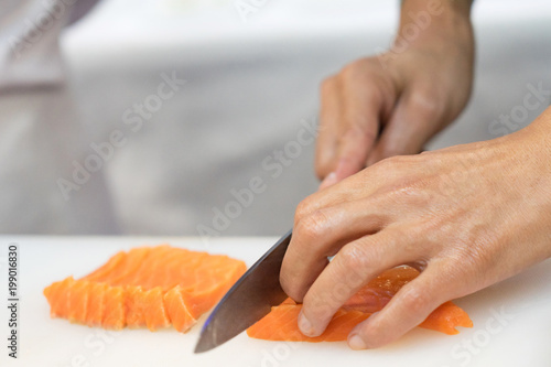 Hand of chef use knife preparing a fresh salmon on a cutting board, Japanese chef in restaurant slicing raw salmon, ingredient for seafood dish
