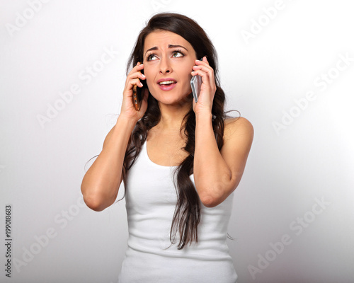 Unhappy doubt thinking stressed woman holding two mobile phones near the ears and looking up on white background