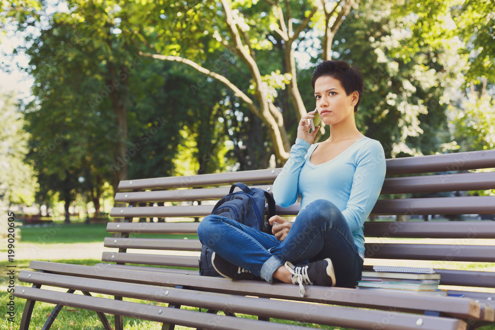 Fototapeta premium Pensive woman speaking on mobile phone in the park