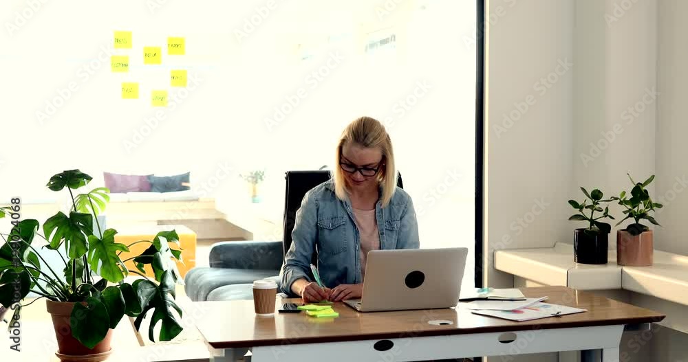 37Casually dressed young businesswoman sitting alone at a desk in an office working on a laptop and writing ideas down on sticky notes 37Casually dressed young businesswoman sitting alone at a desk in an office working on a laptop and writing ideas down on sticky notes