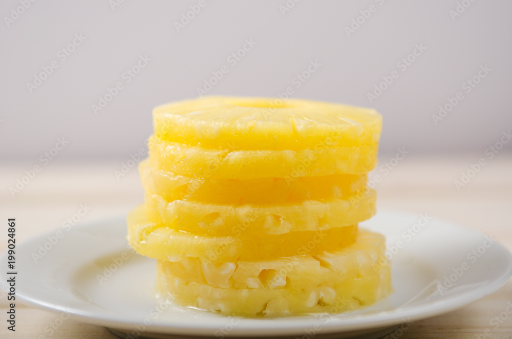 Pieces of pineapple. Pineapple chopped into round pieces in a pile on a white plate on a white wooden background Pieces of pineapple. Pineapple chopped into round pieces in a pile on a white plate on a white wooden background