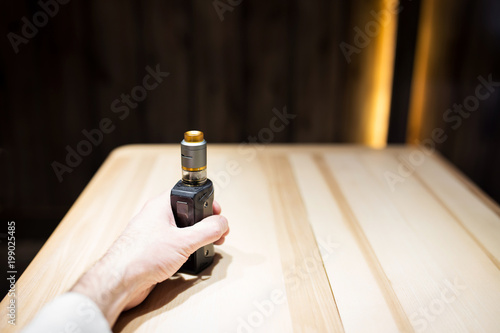 A man's hand holds vape in a cafe, safe smoking