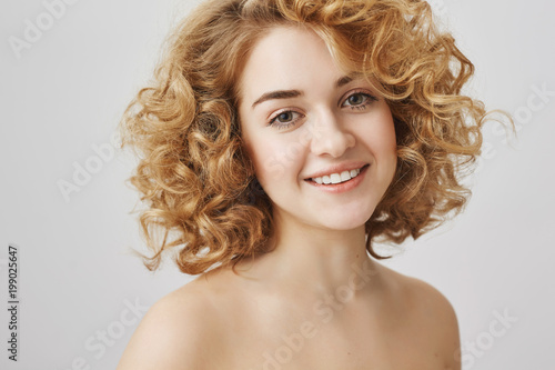 Yes, I sing in shower. Waist-up portrait of charming caucasian female with curly hair standing naked, smiling broadly at camera. Young sportswoman receives massage at spa. Beauty and emotions concept