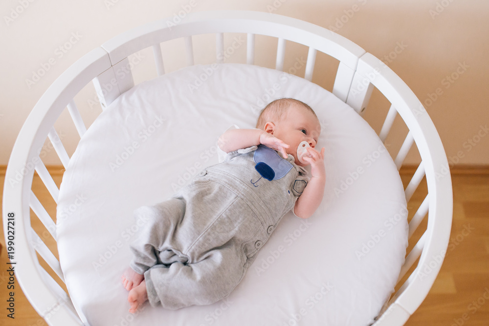 Beautiful newborn baby lying in an round bed with beautiful bumpers in delicate gray, blue, white tones