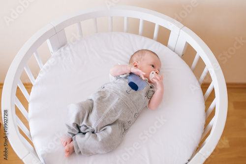Obraz na płótnie Beautiful newborn baby lying in an round bed with beautiful bumpers in delicate gray, blue, white tones w salonie