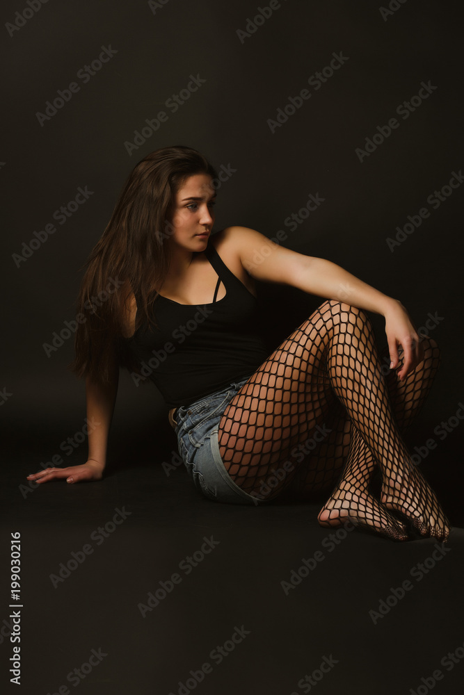 Model test with young glorious model in black shirt and jeans shorts posing in the shadows Model test with young glorious model in black shirt and jeans shorts posing in the shadows