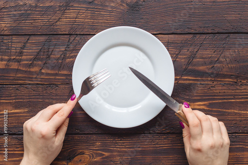 female hands holding fork and knife over the empty plate on dark wooden background