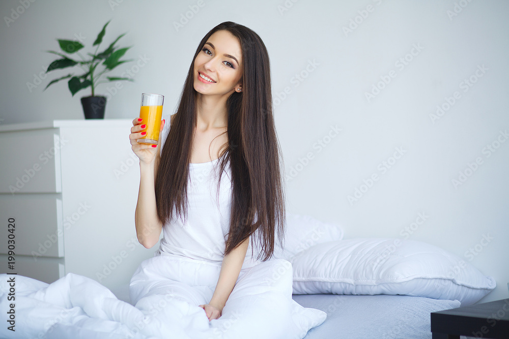 Cheerful woman drinking an orange juice sitting on her bed at home Cheerful woman drinking an orange juice sitting on her bed at home