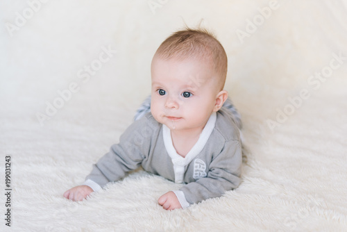 Small baby boy lying on stomach and raising his head awhile looking surprised and smiling cute, newborn