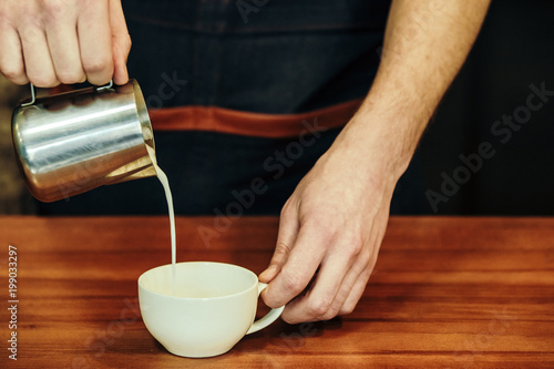 Waiter hands pouring milk making cappuccino