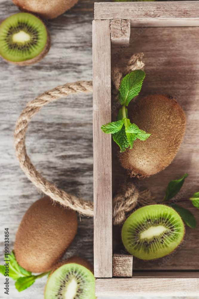 Fototapeta Green kiwis and mint leaves in the wooden tray