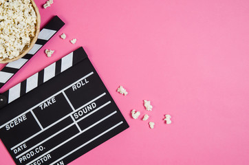 Fresh popcorn and movie clip isolated on pink background top view with copy space around products. Cinematic concept for blogs or design