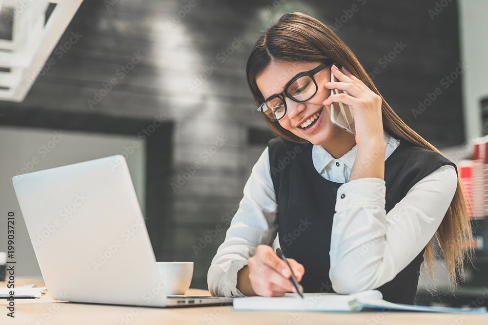 The cute businesswoman in glasses phones at the desktop The cute businesswoman in glasses phones at the desktop