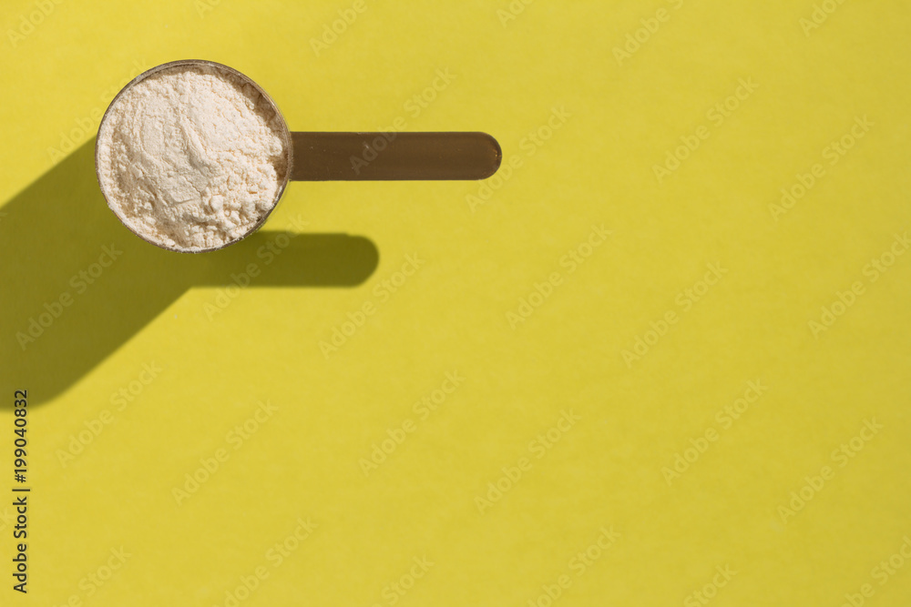 Whey Protein. Minimal concept and hard light. Scoop with vanilla flavoured powder on yellow background. Whey Protein. Minimal concept and hard light. Scoop with vanilla flavoured powder on yellow background.