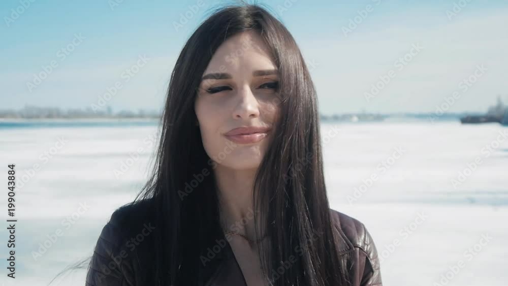 slowmotion portrait of young beautiful brunette woman in winter on a snow background of frozen river slowmotion portrait of young beautiful brunette woman in winter on a snow background of frozen river