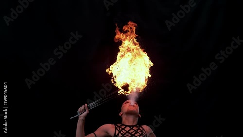 Fire artist entertainer breathes burning flame in the dark