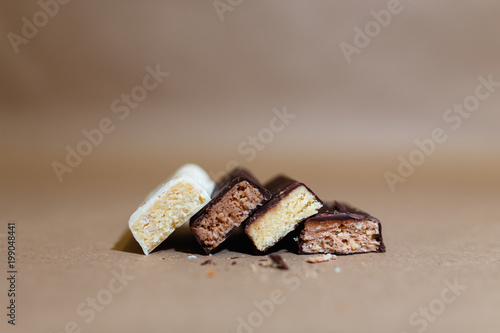 Four chocolate protein bars with different flavors in the context of sprinkle rice flakes on baking paper, Teflon paper. Whey protein powder and chocolate protein bar on wooden background. Text space