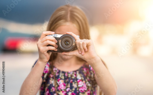 Beautiful little girl with camera takes a picture, summer outdoor