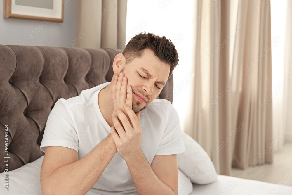 Man suffering from tooth pain in bedroom Man suffering from tooth pain in bedroom