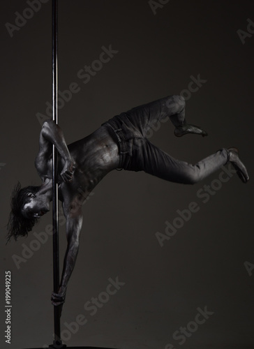 Guy with nude torso performing pole dancing moves on pole. © Volodymyr