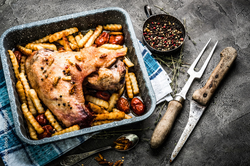 Homemade turkey wing with french fries and spices in baking tray with knife and fork carving set on gray table
