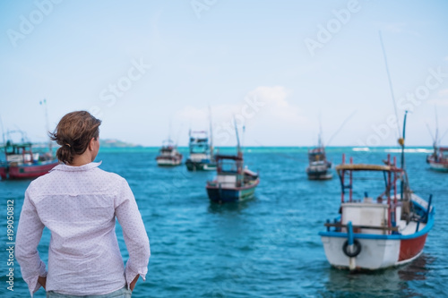 Caucasian woman standing on the beach of Midigama and looking on ocean and traditional colourful local boats, Travelling in Asia on vacation,