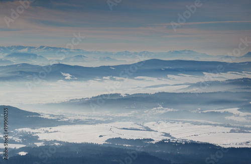 Sunlit winter scenery elevated view with blue mountain ridges, snowfields in misty valleys and Low Tatras in the distance, Orava and Liptov regions Oravska Magura Chocske vrchy ranges Slovakia Europe © nogreenabove2k