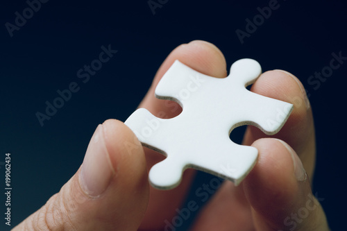 Discover solution or strategy missing piece for business success concept, hand holding a bright white paper jigsaw puzzle piece with dark black background