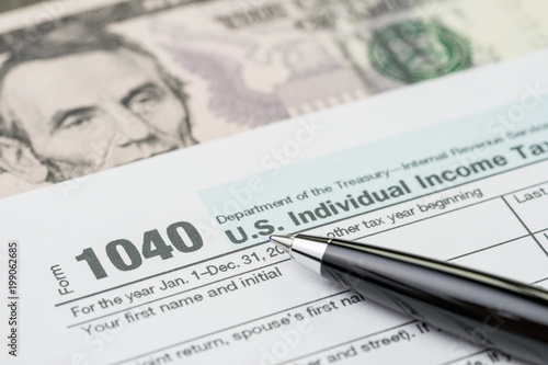 Tax time concept, pen on 1040 US individual income tax filling form with US dollar bill, calculate from yearly revenue to pay the government