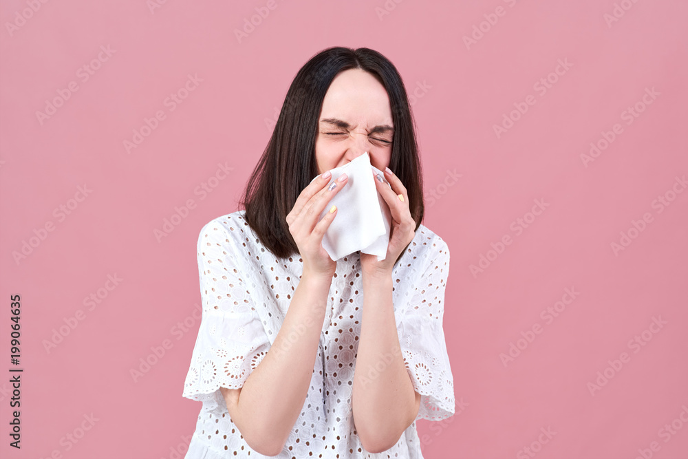 Studio portrait of a young white-skinned woman sneezing in a napkin strongly stiffened his eyes and leaning. Studio portrait of a young white-skinned woman sneezing in a napkin strongly stiffened his eyes and leaning.