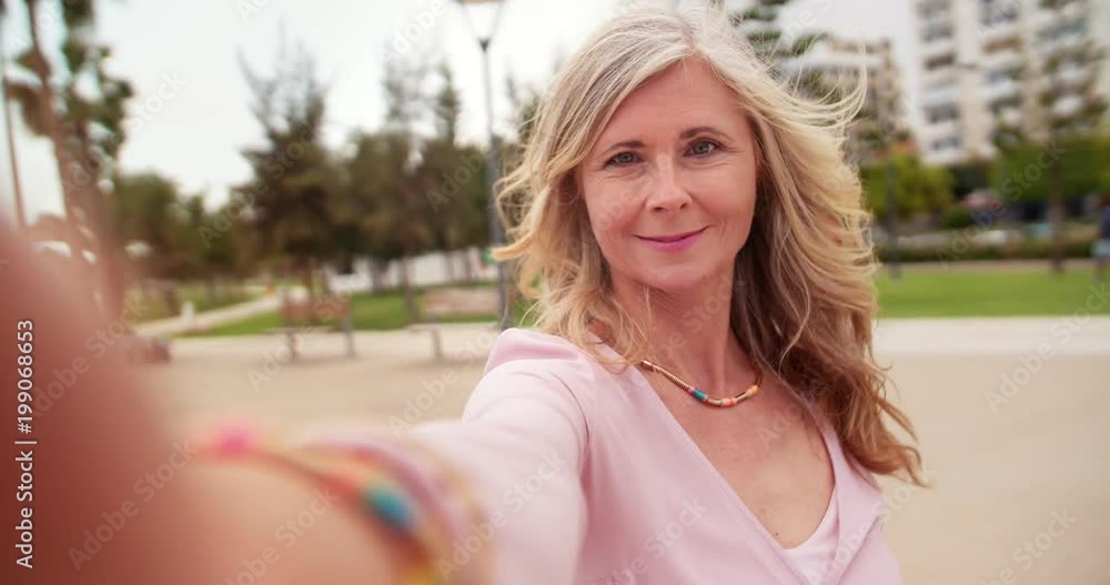 Beautiful senior woman taking selfies on a smartphone in park Beautiful senior woman taking selfies on a smartphone in park