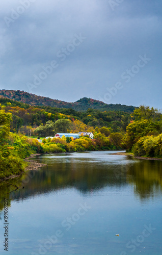 Reflection of a still river in Vermont during peak fall foliage season with a farm in the distance
