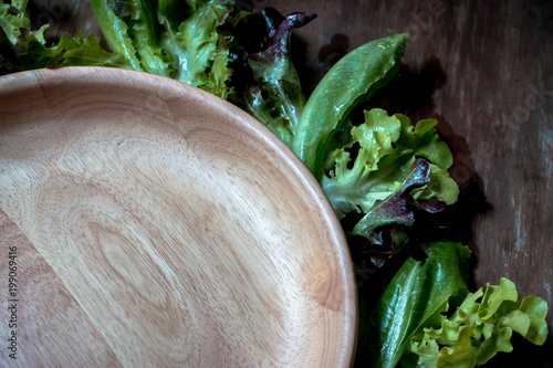 A wood tray surround with green salad on the wooden table. A bowl of green salad a day make good health benefits. Vegetables in salads are good sources of fiber. photo