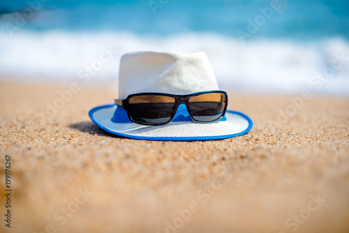 Beach hat and sunglasses lying on the sand by the sea 