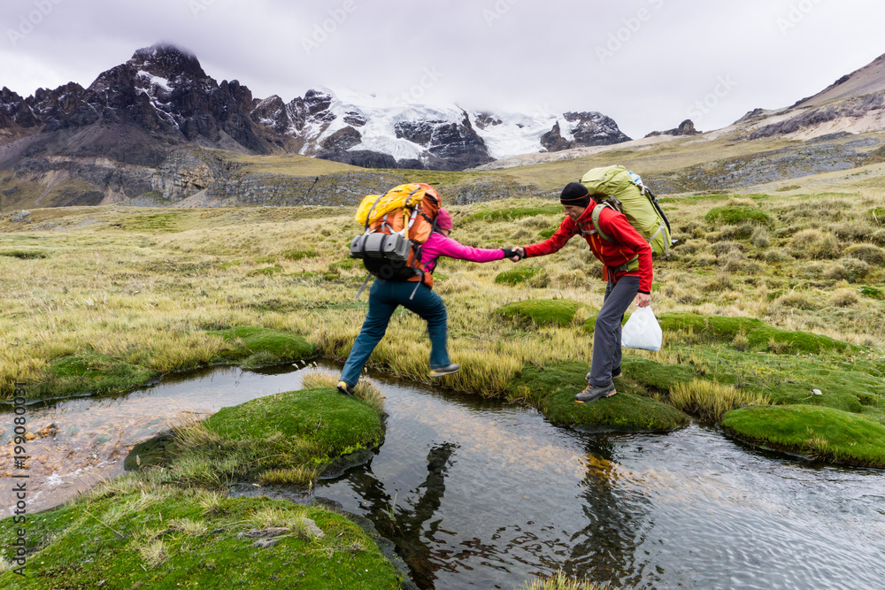Obraz premium male mountain climber helps his female partner cross a small mountain stream high up in the Cordillera Blanca in the Andes in Peru