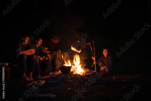 children with his father at night in the forest by the fire.
