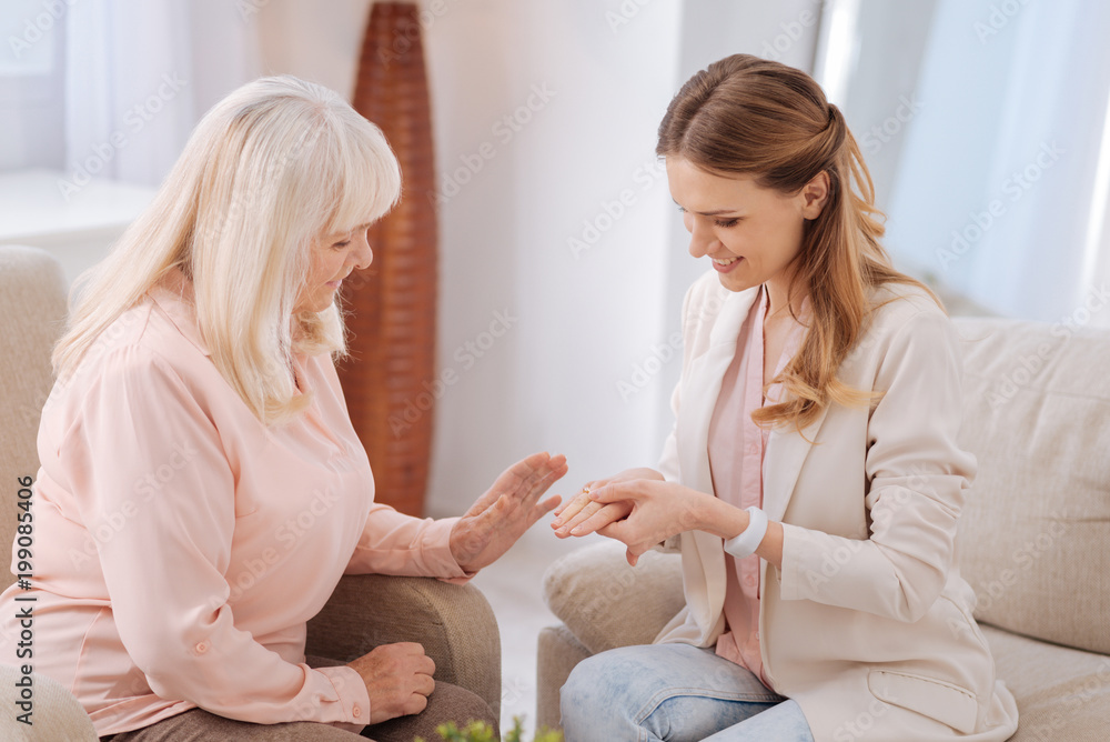 Obraz premium Future wife. Positive joyful nice woman sitting opposite her mother and showing her the ring while telling about the engagement