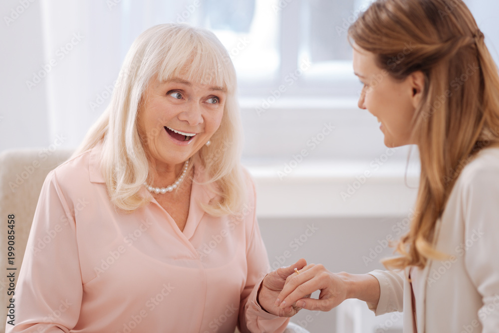 Important life event. Delighted nice cheerful woman smiling and looking at her daughters engagement ring while feeling excited about this event