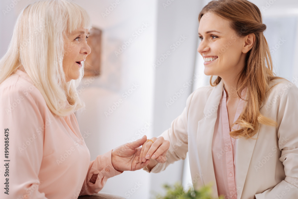 Happy event. Positive nice senior woman smiling and looking at her daughters engagement ring while being happy for her Happy event. Positive nice senior woman smiling and looking at her daughters engagement ring while being happy for her