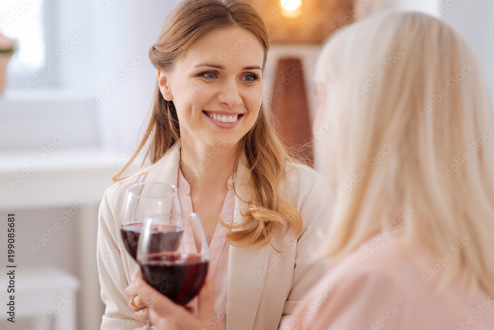 Female drink. Happy nice beautiful woman smiling and looking at her mother while having wine with her Female drink. Happy nice beautiful woman smiling and looking at her mother while having wine with her