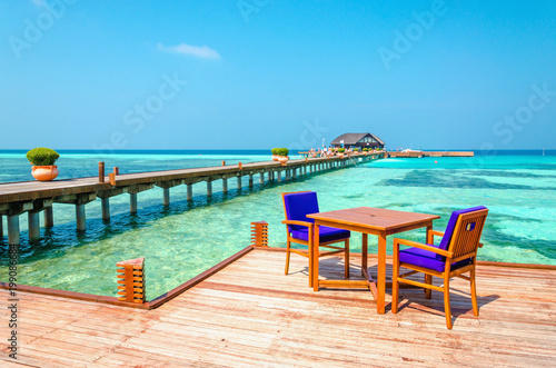 Tables and chairs in a wooden restaurant on stilts on the background of azure water and blue sky