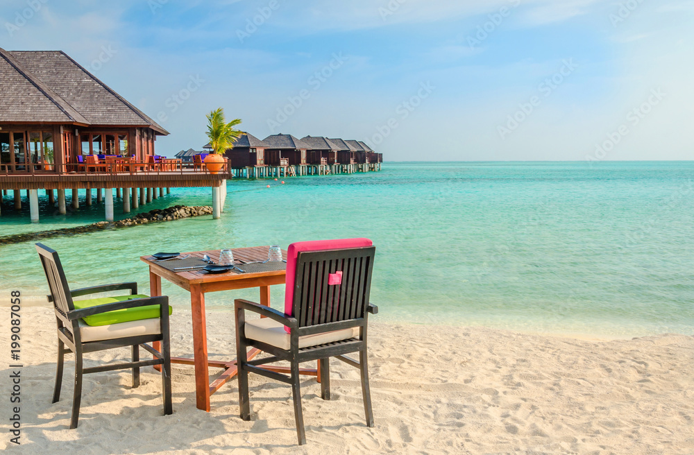 Obraz premium Table and chairs at restaurant at the background of water bungalows, Maldives