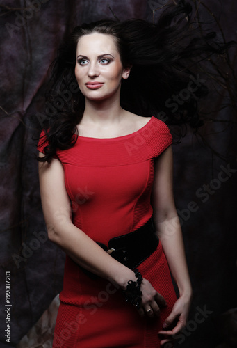 Beautiful brunette in a red dress posing on a theatrical background