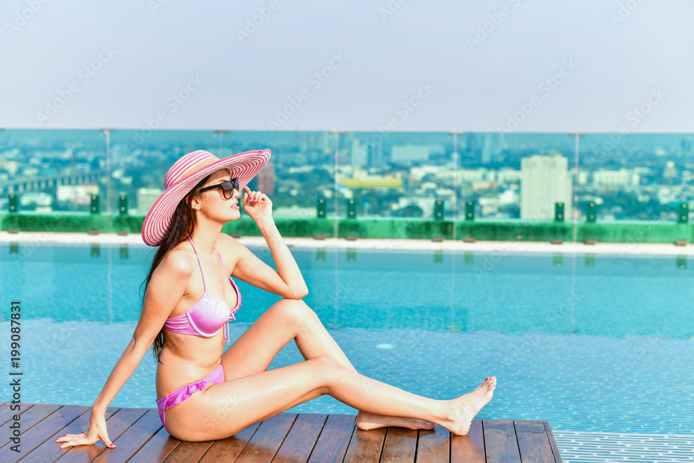 Swimsuit Concept. Beautiful girl wearing pink swimsuit. Beautiful girl in swimwear is relaxing at the swimming pool. Independent living sexy woman at the city center pool.