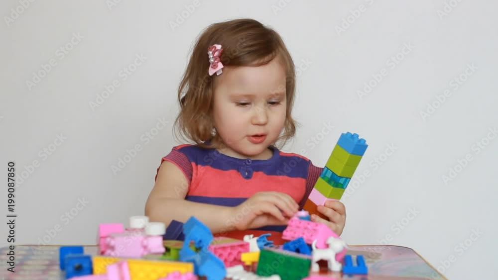 Little baby playing with colourful small blocks of a constructor. The child develops his thinking and motor skills. A sweet girl is busy building. Entertainment and games for children. Development and Little baby playing with colourful small blocks of a constructor. The child develops his thinking and motor skills. A sweet girl is busy building. Entertainment and games for children. Development and